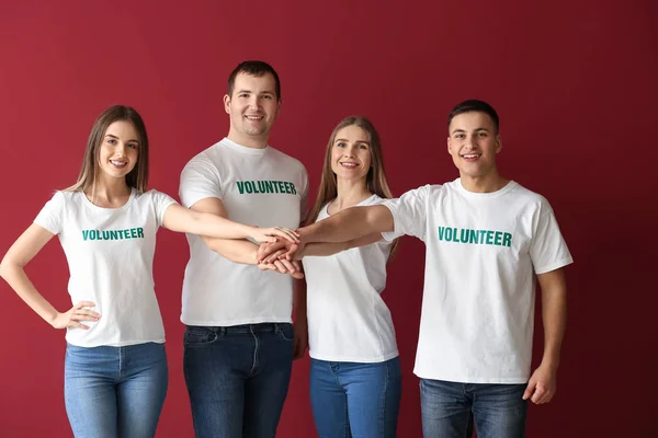 Young volunteers putting hands together on color background — Stock Photo, Image
