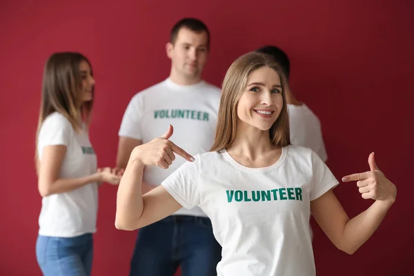 Young female volunteer and her team on color background