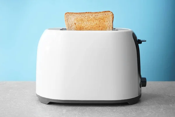 Slice of bread with toaster on table against color background — Stock Photo, Image