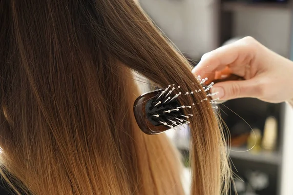 Парикмахер расчесывает длинные волосы молодой женщины в салоне — стоковое фото