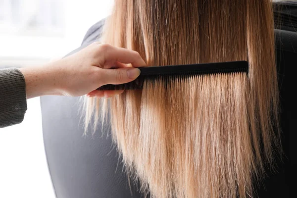 Перукар розчісує довге волосся молодої жінки в салоні — стокове фото