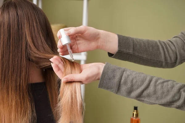 Hairdresser applying serum onto hair of young woman in salon — Stock Photo, Image