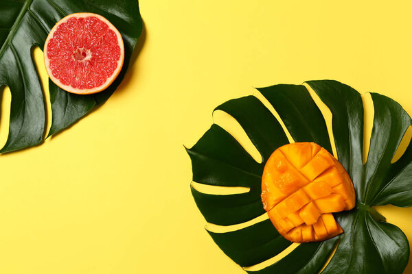 Вкусные экзотические фрукты с тропическими листьями на цветном фоне
