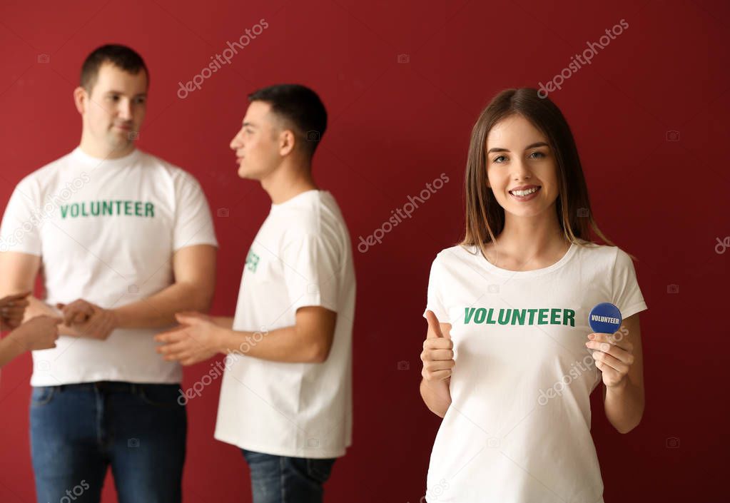 Young female volunteer and her team on color background