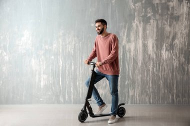 Tekme scooter gri duvarının yakınında şık genç adam