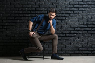 Karanlık tuğla duvara yakın oturan moda genç adam