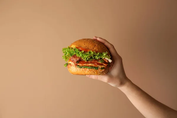 Weibliche Hand mit leckerem Burger auf farbigem Hintergrund — Stockfoto