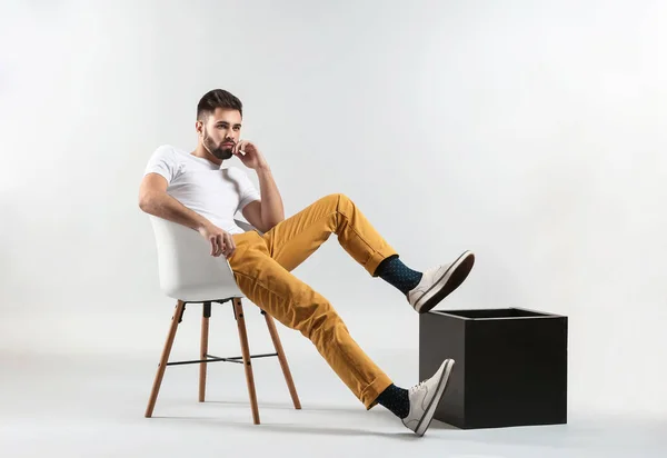 Jovem elegante sentado na cadeira contra fundo leve — Fotografia de Stock