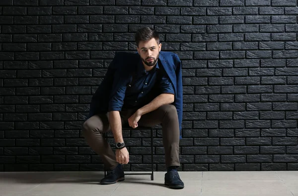 Elegantní mladý muž sedí poblíž tmavě cihlová zeď — Stock fotografie