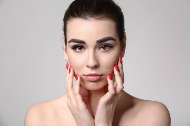 Gri arka planda güzel kaşları olan genç bir kadın.