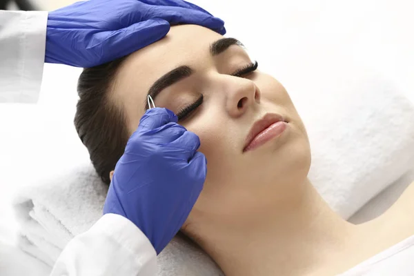 Young woman undergoing eyebrow correction procedure in beauty salon