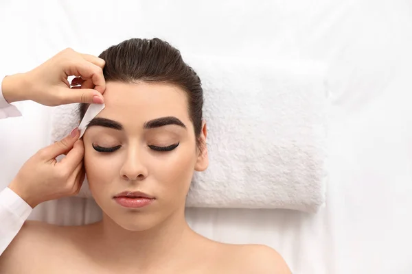 Young woman undergoing eyebrow correction procedure in beauty salon