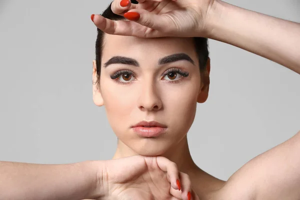 Young woman with beautiful eyebrows on grey background