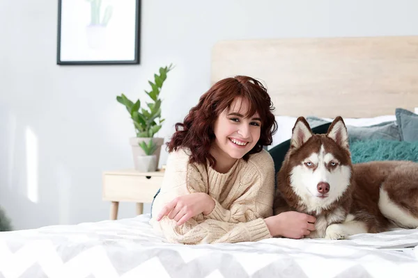 Jovem mulher com seu cão bonito deitado na cama em casa — Fotografia de Stock