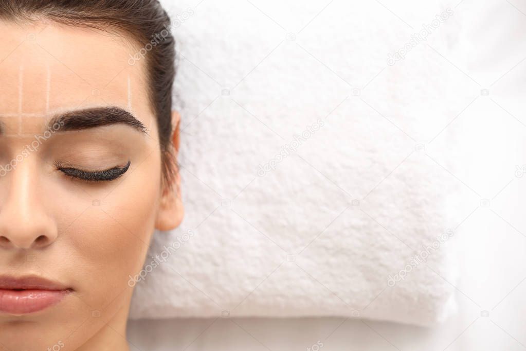 Young woman undergoing eyebrow correction procedure in beauty salon