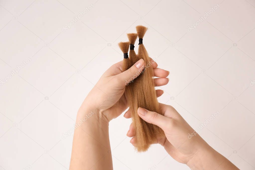 Female hands with hair strands on light background. Concept of donation