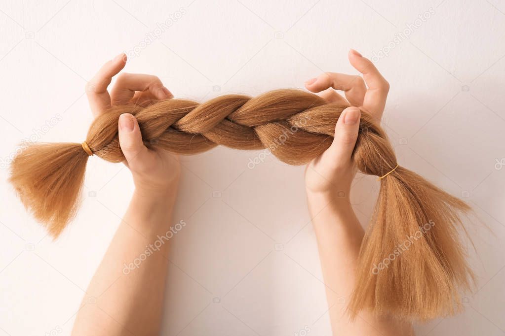 Female hands with braided strand on light background. Concept of hair donation
