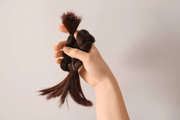 Mão feminina com fio trançado no fundo claro. Conceito de doação de cabelo — Fotografia de Stock