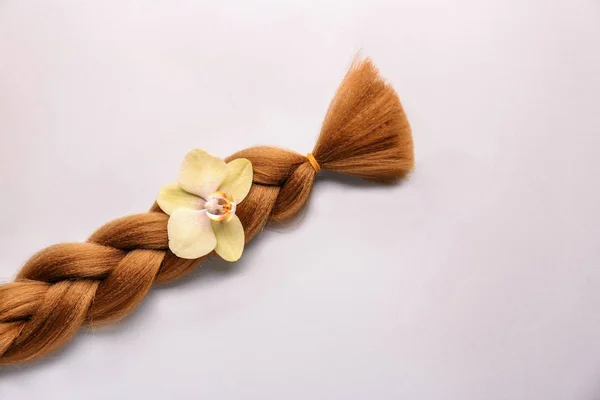 Πλεγμένες strand και λουλούδι σε ανοιχτόχρωμο φόντο. Έννοια της δωρεάς μαλλιών — Φωτογραφία Αρχείου