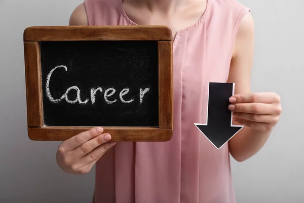 Woman holding chalkboard with word CAREER and arrow directed downwards. Concept of career failure — Stock Photo, Image