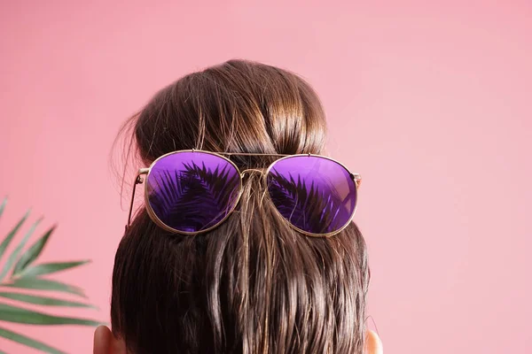 Young woman with hair bun and sunglasses on color background