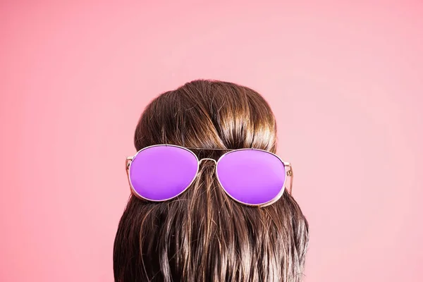 Young woman with hair bun and sunglasses on color background