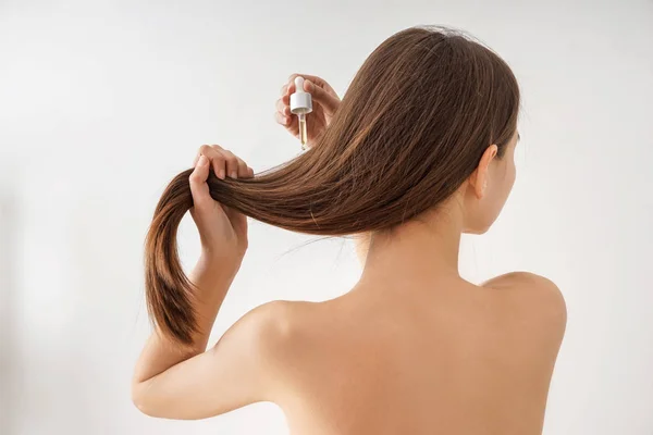 Woman using cosmetics for hair care on white background