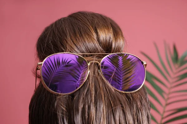 Mujer joven con moño de pelo y gafas de sol sobre fondo de color —  Fotos de Stock