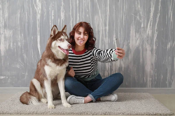 Young woman taking selfie with her cute dog near grey wall — Stock Photo, Image