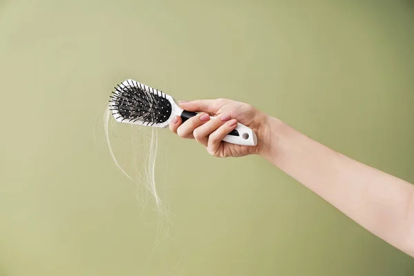 Mão de mulher com problema de perda de cabelo segurando escova no fundo de cor — Fotografia de Stock