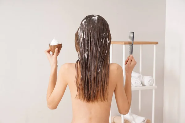 Femme utilisant de l'huile de coco pour les cheveux dans la salle de bain — Photo