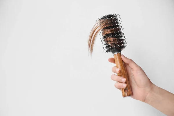 Mano de mujer con problemas de pérdida de cabello sosteniendo cepillo sobre fondo claro — Foto de Stock