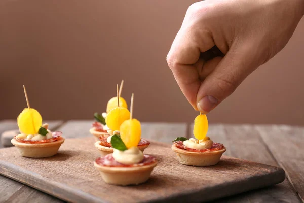 Female hand with tasty canapes on wooden board — Stock Photo, Image