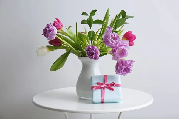 Buquê de flores bonitas com caixa de presente na mesa contra fundo claro — Fotografia de Stock