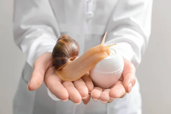 Cosmetólogo sosteniendo caracol gigante Achatina y cosméticos con mucina, primer plano — Foto de Stock