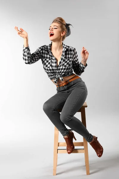 Schöne Pin-up-Frau sitzt auf Hocker vor grauem Hintergrund — Stockfoto