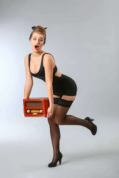 Surprised pin-up woman with radio receiver on grey background