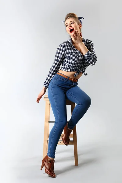 Beautiful pin-up woman sitting on stool against grey background — Stock Photo, Image
