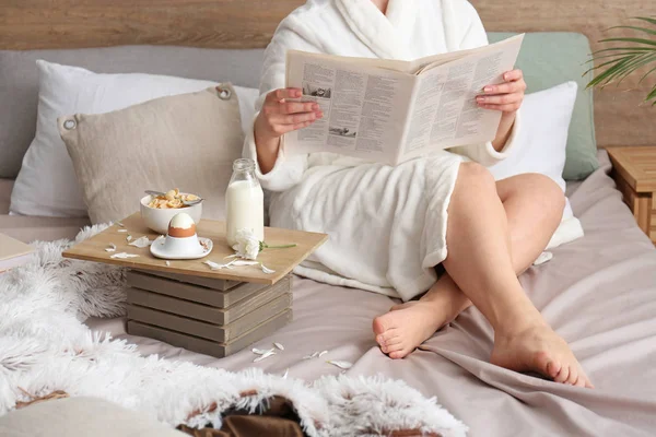 Young woman reading newspaper and having breakfast in bed — Stock Photo, Image