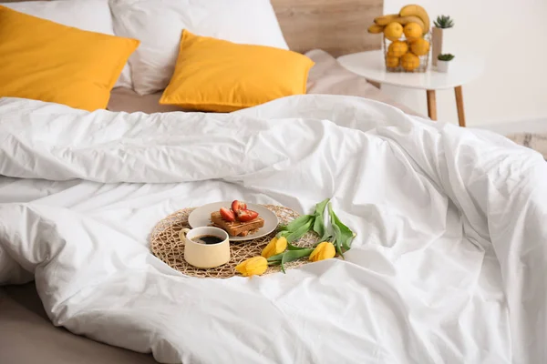 Tasty healthy breakfast and flowers on bed — Stock Photo, Image