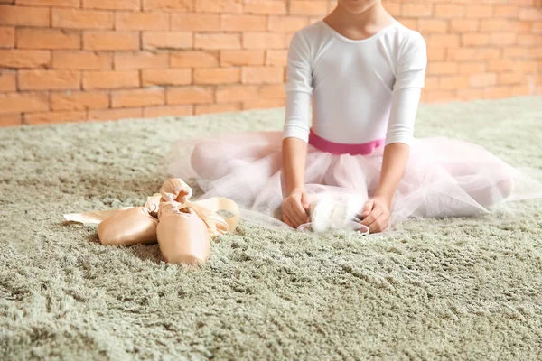 Schattige kleine ballerina nabij point schoenen zitten op zacht tapijt — Stockfoto