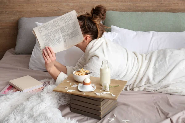 Jovem mulher lendo jornal e tomando café da manhã na cama — Fotografia de Stock