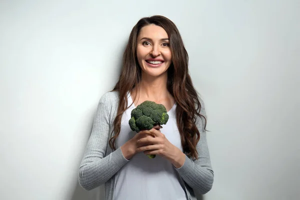 Woman with fresh broccoli on light background — Stock Photo, Image