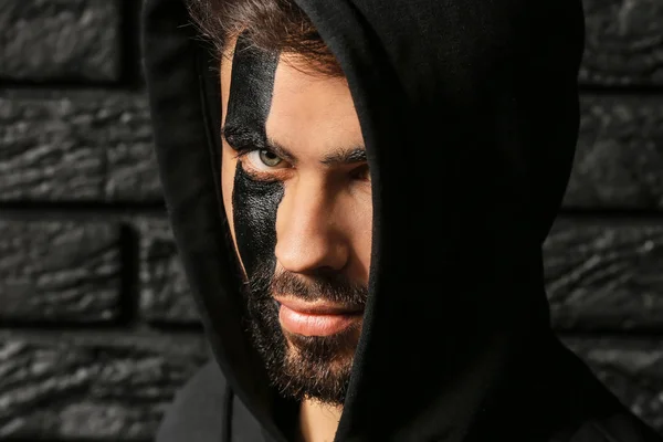 Портрет красивого мужчины с краской на лице на темном кирпичном фоне — стоковое фото