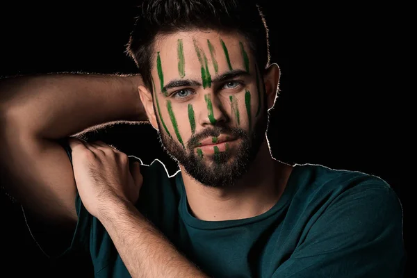 Portrait of handsome man with paint on his face against dark background — Stock Photo, Image