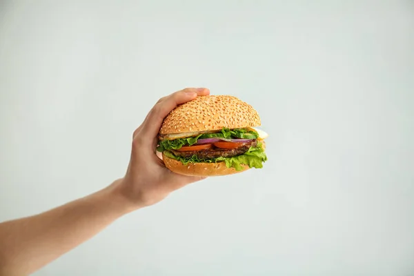 Mano femenina con sabrosa hamburguesa fresca sobre fondo claro — Foto de Stock