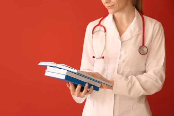 Female doctor with books on color background