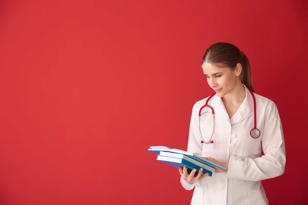 Female doctor with books on color background — Stock Photo, Image
