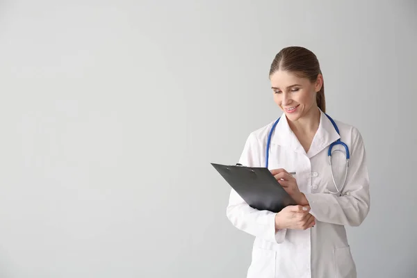 Female doctor with clipboard on light background — Stock Photo, Image