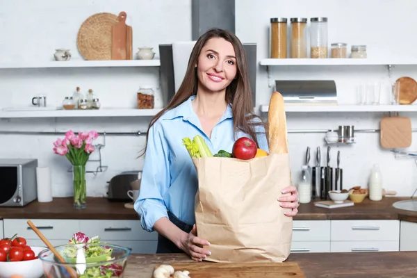 Hermosa mujer con bolsa llena de productos en la cocina en casa —  Fotos de Stock
